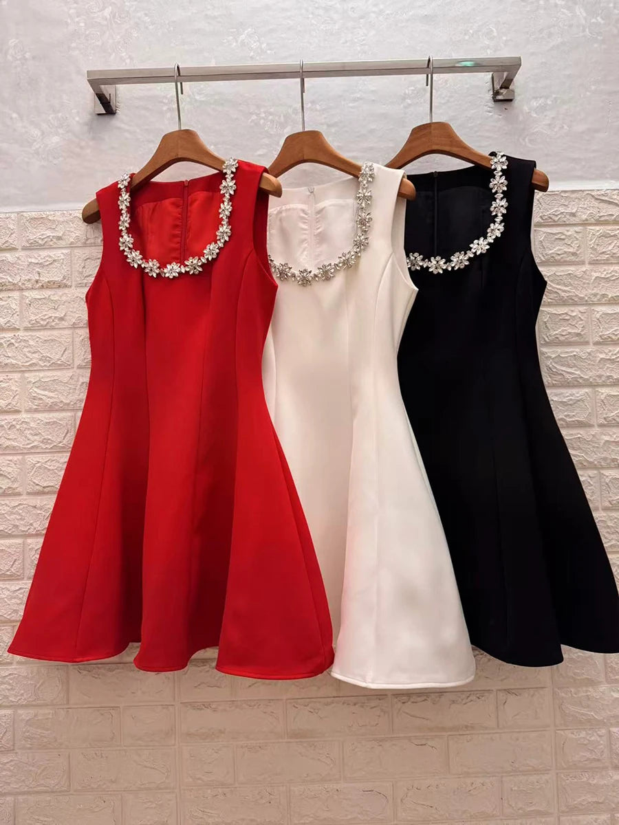 Three dresses in red, white, and black hanging on a rack against a brick wall.