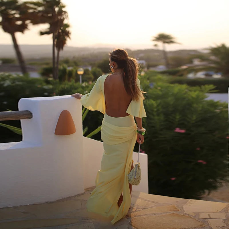 Woman in a yellow dress standing on a balcony with a scenic view.