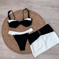 Two people posing on a beach, one wearing a black and white contrast trim bikini and skirt ensemble.
