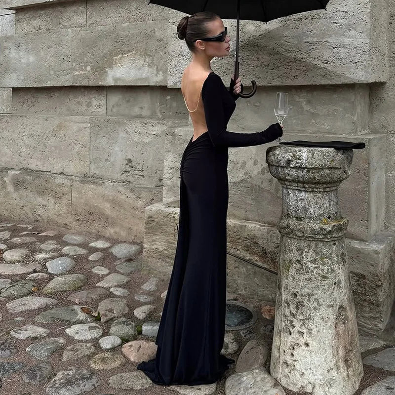 Woman in a black evening gown holding an umbrella and a glass against a stone wall.
