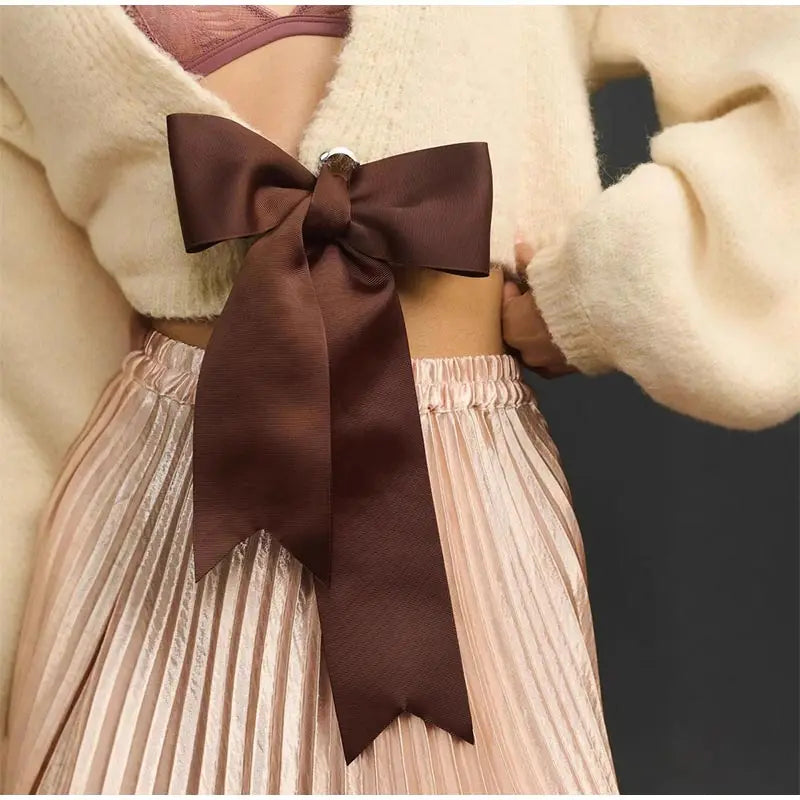 Close-up of a brown bow on a beige sweater and pleated skirt against a dark background