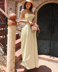 Woman in a long light dress and hat standing outdoors near stone steps.