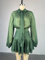 Green dress with long sleeves and a tie neckline on a mannequin against a gray background