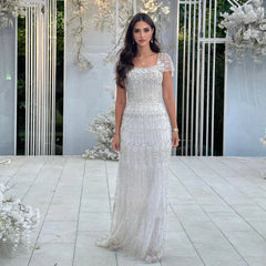 Woman in a white beaded gown standing in a decorated outdoor setting with floral arrangements.