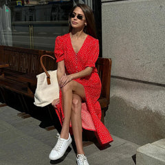 Woman in a red dress with white polka dots sitting on a bench wearing sunglasses.