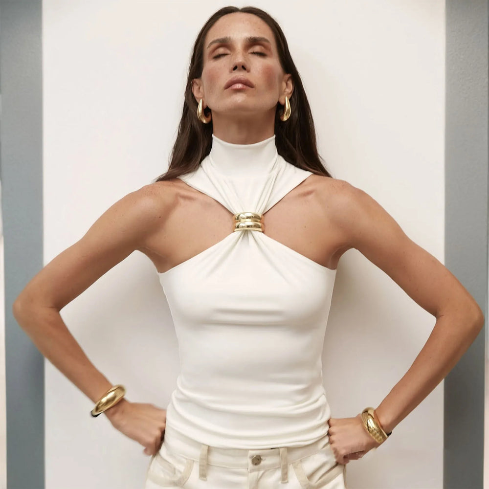 Woman wearing a white halter top with a gold accent against a plain background