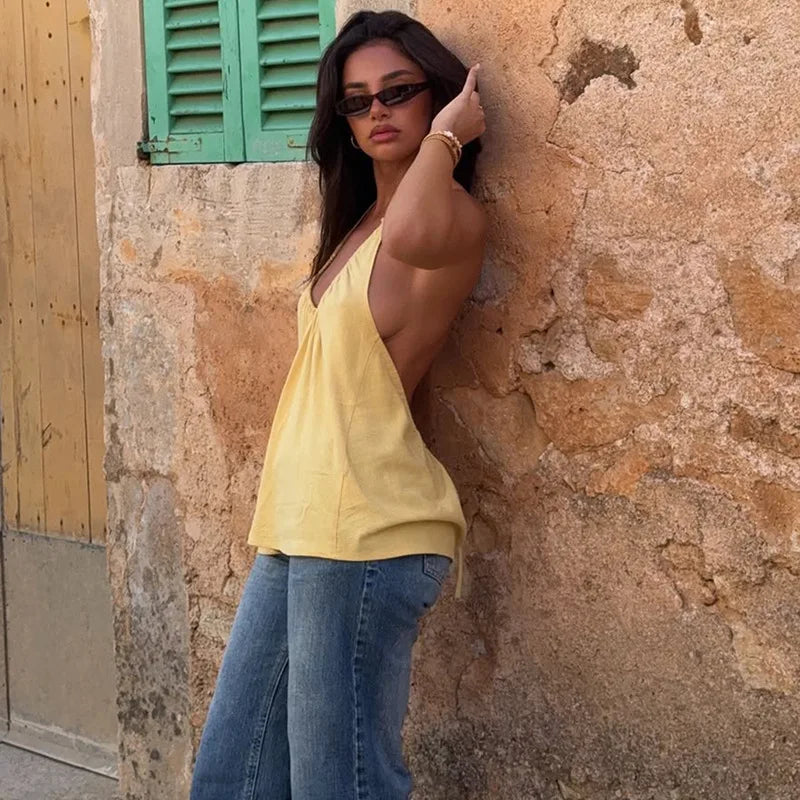 Woman in yellow top and blue jeans leaning against a stone wall.