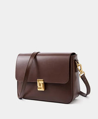 Brown leather handbag with a gold clasp on a light gray background