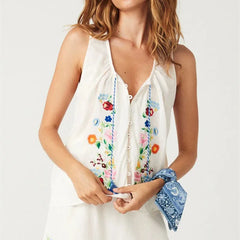 Woman wearing a white sleeveless top with colorful floral embroidery on a plain background