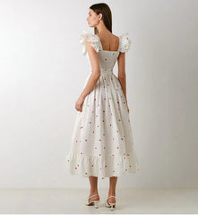 Woman wearing a white dress with floral details on a plain background