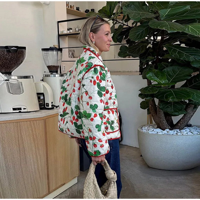 Person wearing a colorful quilted jacket in a kitchen setting with a plant and appliances.