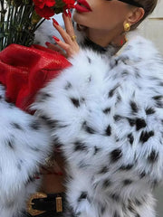 Person wearing a white fur coat with black spots, holding red flowers.