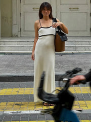 Woman in a long white dress standing on a street with a bicycle in the foreground.