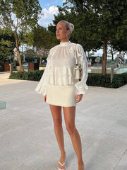 Woman in a white outfit standing outdoors with trees and a clear sky in the background