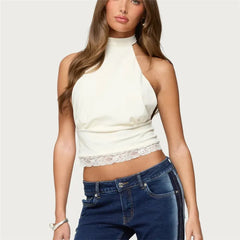 Woman wearing a white halter top with lace detail and blue jeans on a plain background