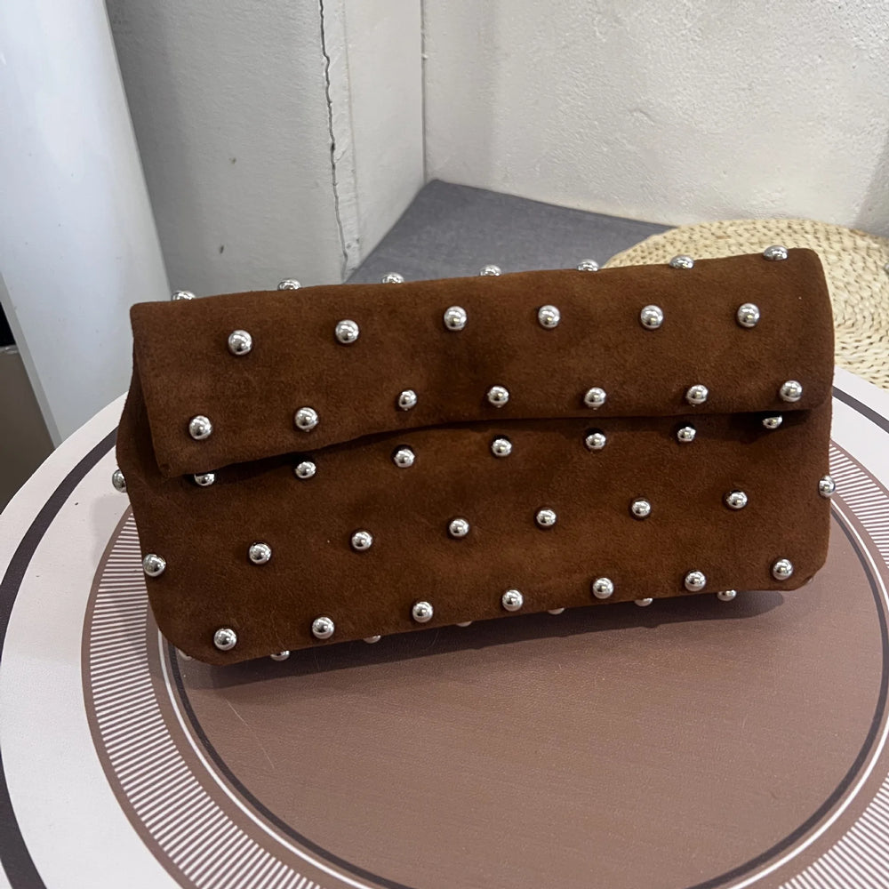 Brown clutch bag with silver studs on a round surface