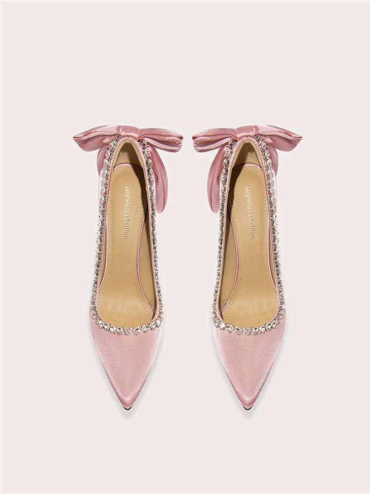 Pink high-heeled shoes with bow details and rhinestone embellishments on a light gray background