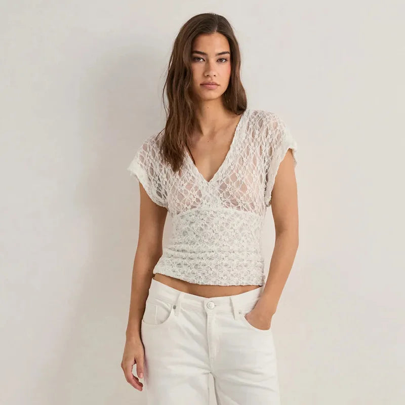 Woman wearing a white lace top and white pants against a plain background