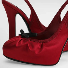 Close-up of a red satin slingback platform pump showing the bow detail.