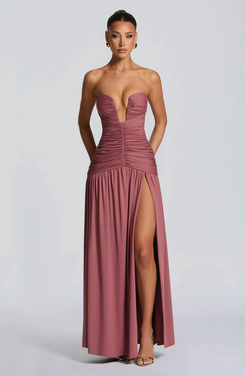 Woman wearing a strapless, long, mauve dress with a high slit on a light gray background