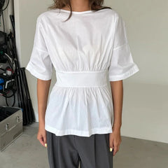 Person wearing a white blouse with a belt and gray pants in an indoor setting