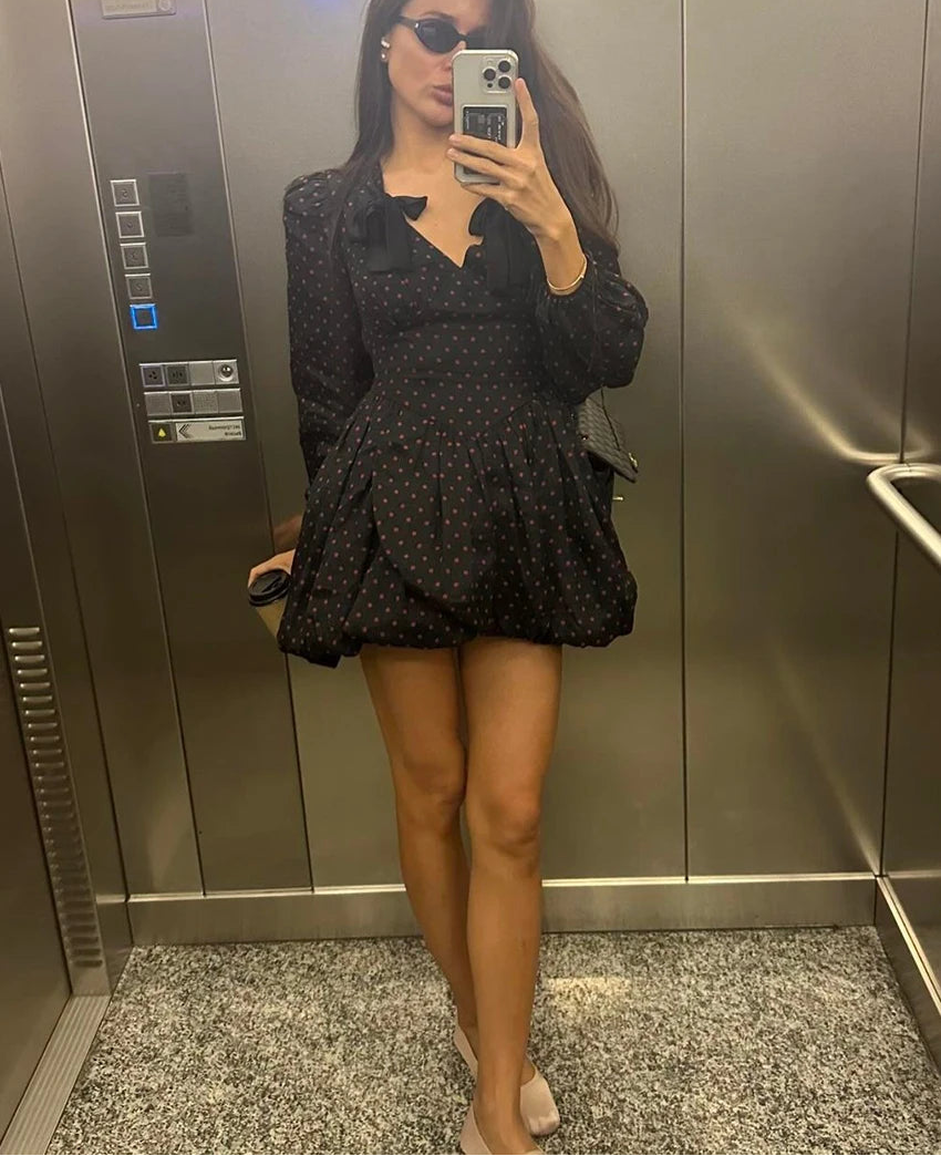 Person taking a mirror selfie wearing a black polka dot dress in an elevator.