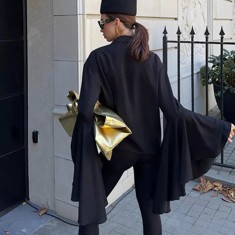 Person wearing a black coat and holding a gold clutch, standing on a sidewalk.