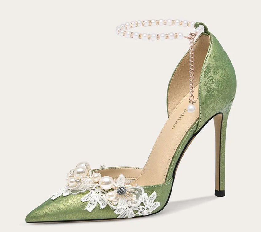 Green high-heeled shoe with floral and pearl details on a light beige background