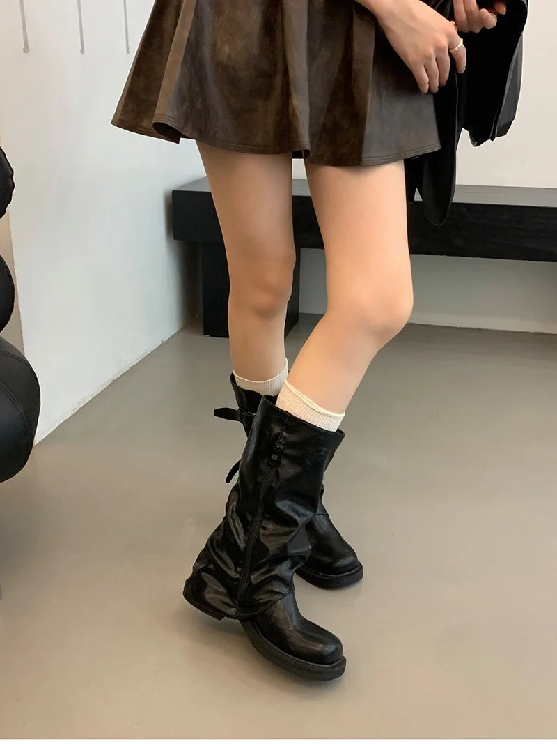 Person wearing black knee-high boots with a plain background