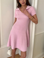 Woman wearing a pink pleated dress against a white wall.