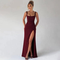 Woman wearing a burgundy evening gown with a high slit on a plain background