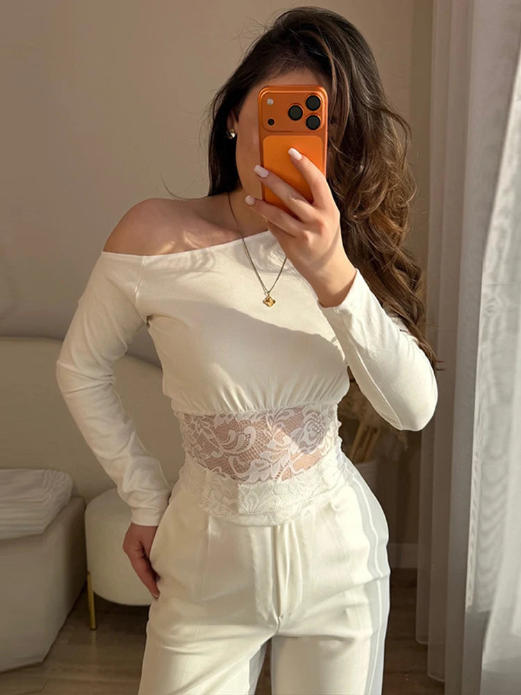Person wearing a white off-shoulder top with lace details and white pants, holding an orange phone.