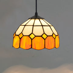 Golden Atelier pendant light featuring a handcrafted Tiffany glass shade with colorful stained glass panels, casting a warm glow. The light hangs from a chain on a ceiling in a living room setting. C