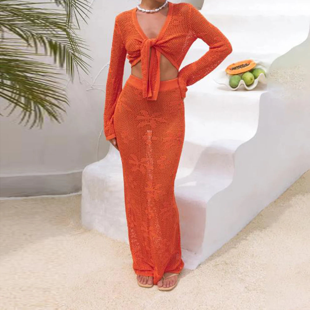 Person wearing an orange knit outfit sitting on a white bench with a plant and fruit bowl in the background.