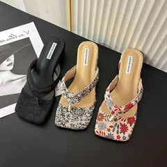 Three pairs of floral and plain sandals on a black surface with a blurred magazine in the background.
