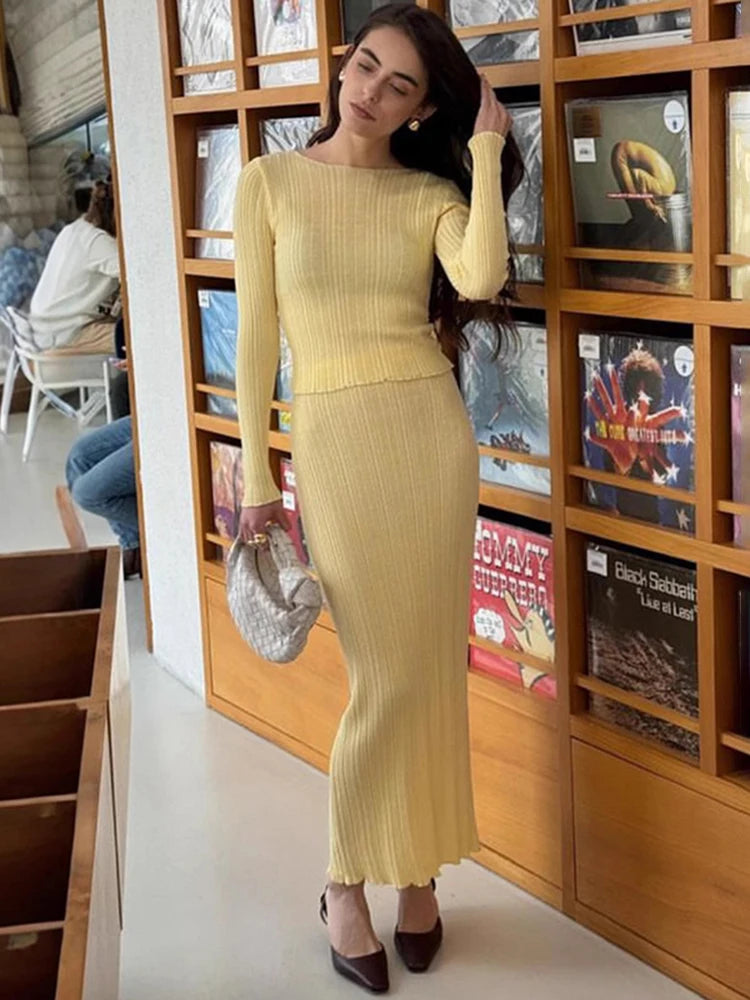 Woman in a yellow dress standing in front of a bookshelf with books and decorative items.