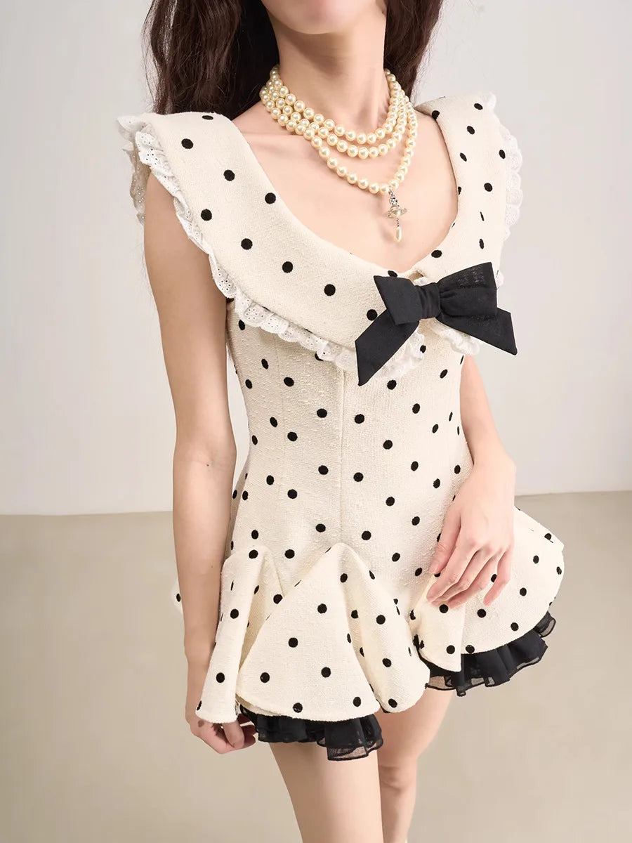 Woman wearing a polka dot dress with a black bow and pearl necklace on a plain background