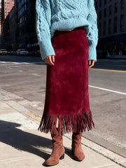 Person wearing a turquoise sweater, red fringed skirt, and brown boots on a city street.