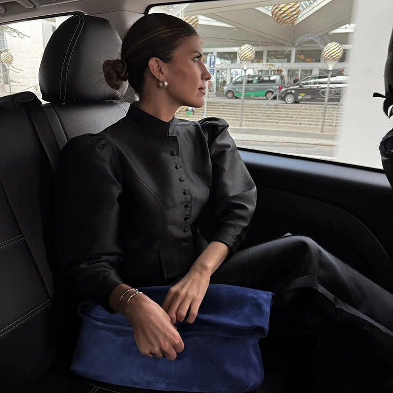 Woman sitting in a car wearing a black outfit with a blue skirt.