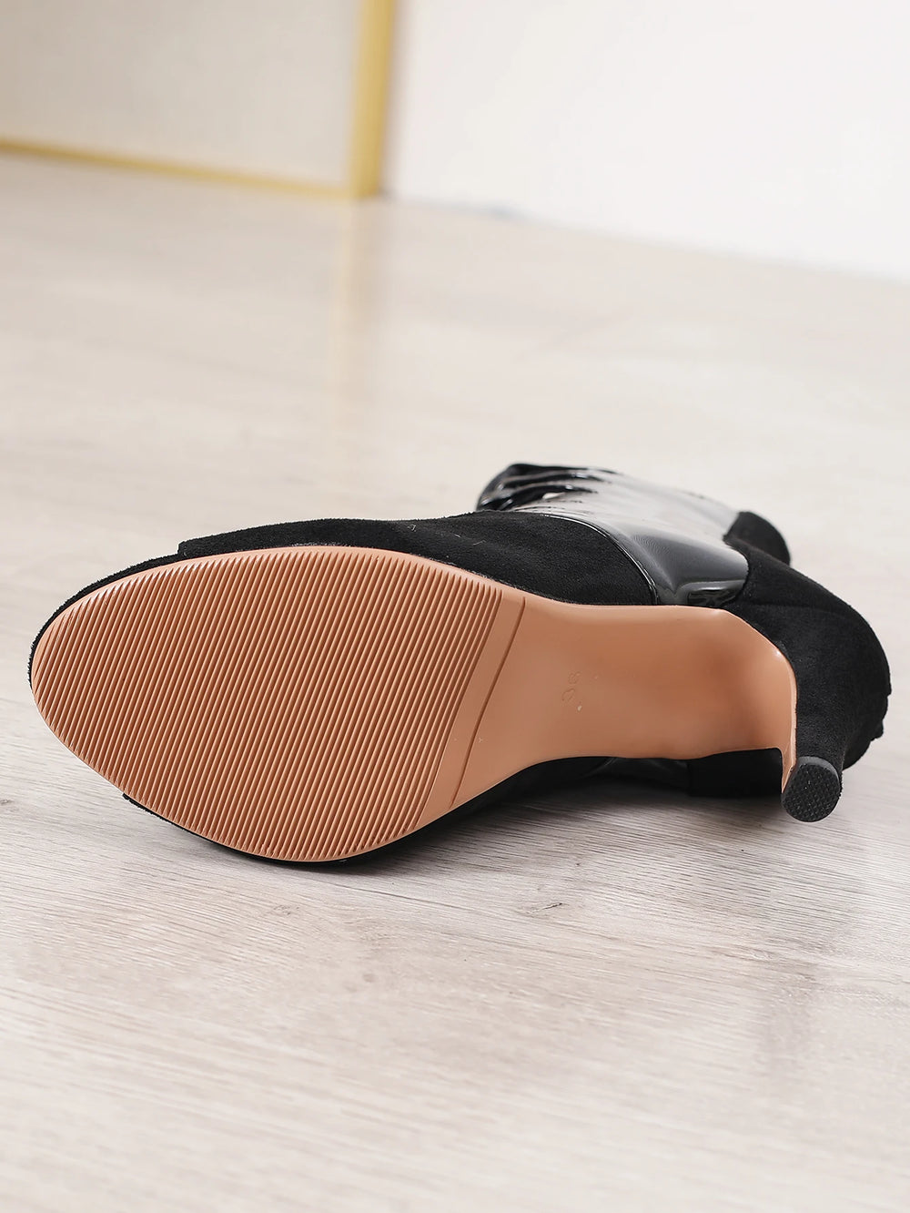 Black shoe with brown sole on a light wooden floor