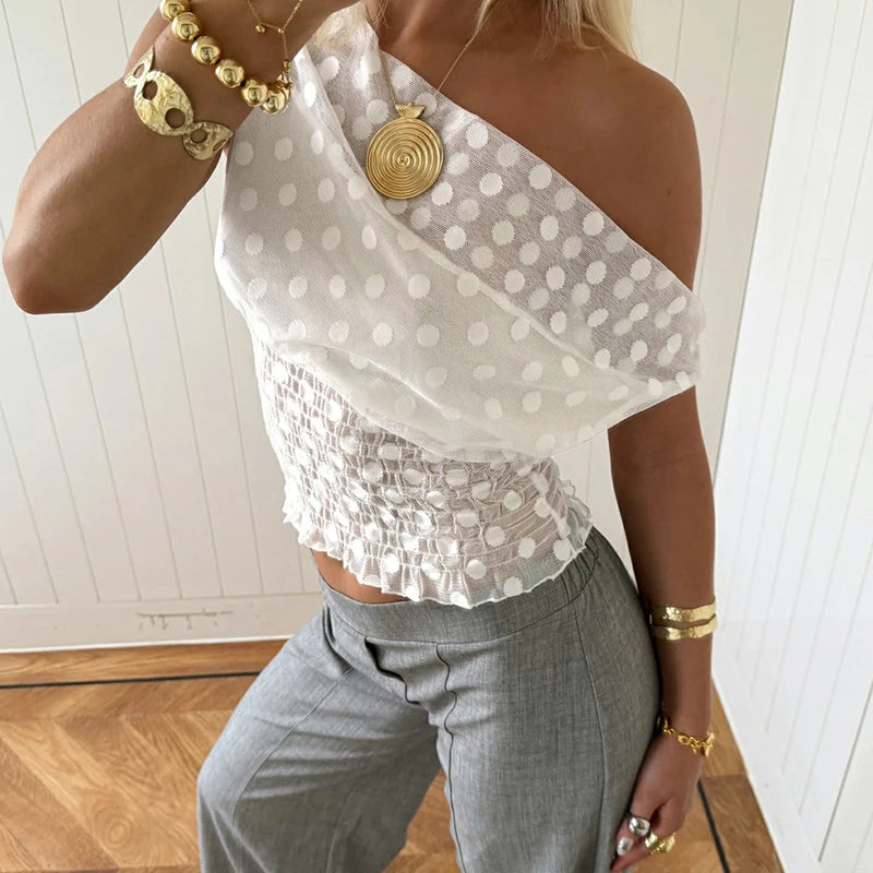 Person wearing a white polka dot top and gray pants with gold jewelry.