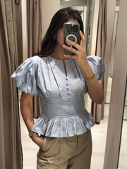 Person wearing a light blue ruffled top taking a mirror selfie.