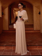 Woman in a long white dress holding a glass of red wine in an indoor setting with arched doorways.