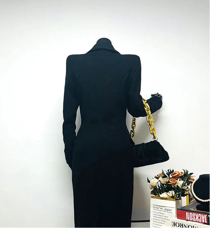Black coat displayed on a mannequin against a white background with a gold handbag.