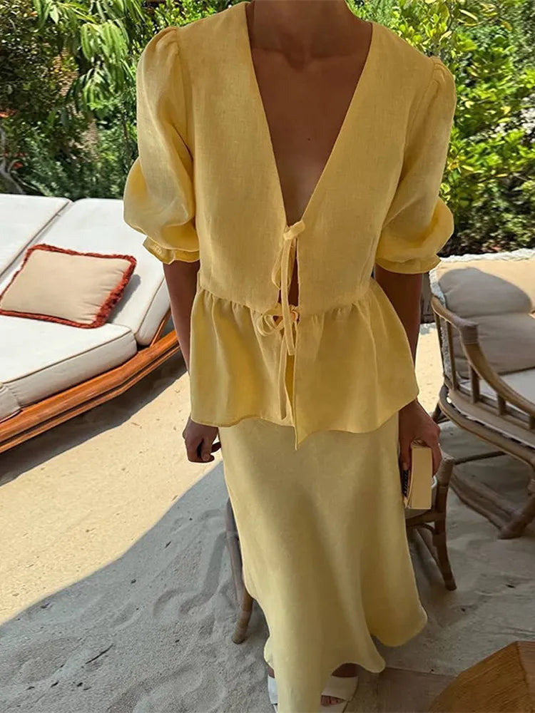 Person wearing a yellow outfit standing on a sandy surface with greenery in the background