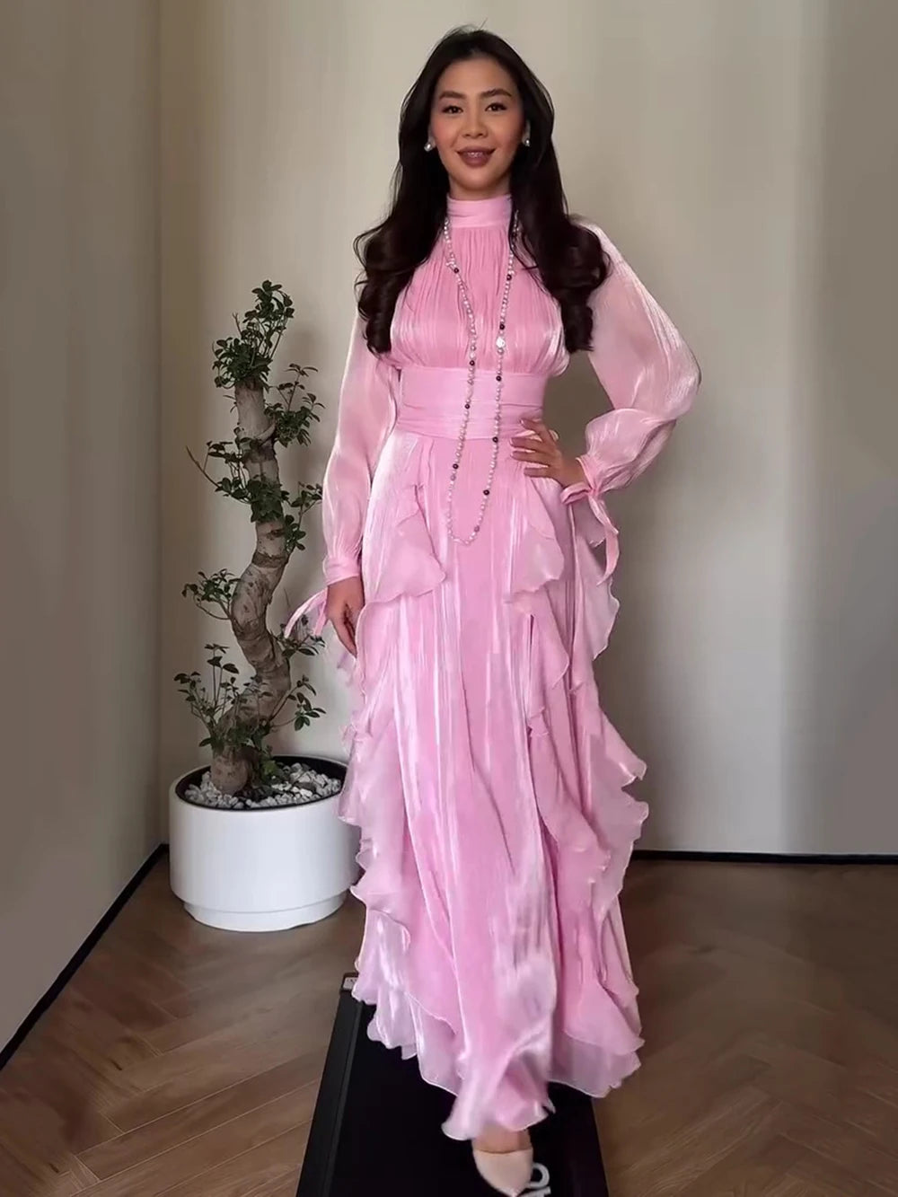 Woman in a pink dress standing indoors with a plant in the background