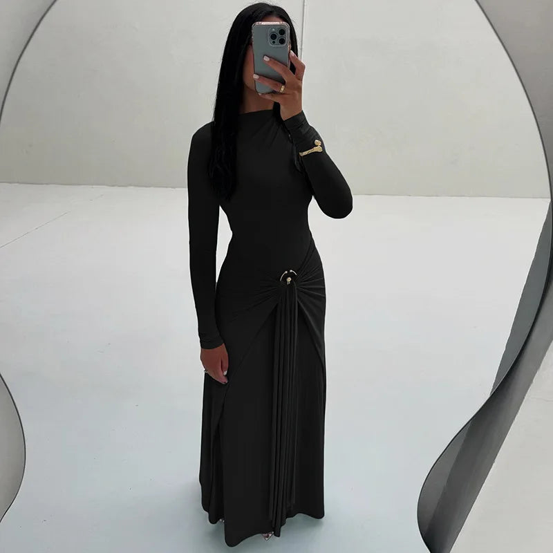 Person wearing a black dress with long sleeves and a slit, standing against a white background.