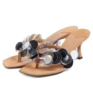 Beige heeled thong sandals with black and silver circular sequin embellishments.