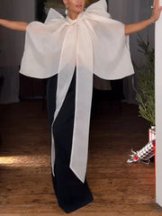 Sheer organza turtleneck top with a large bow and voluminous sleeves, paired with black trousers.