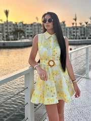 Woman in a yellow floral dress standing by a waterfront at sunset.